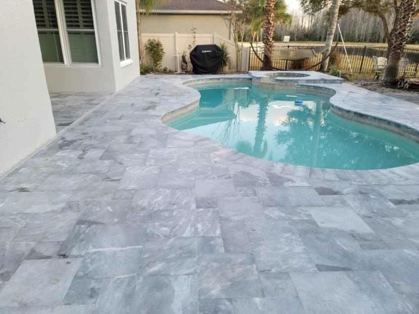 Backyard pool with light blue water and gray stone patio beside a house