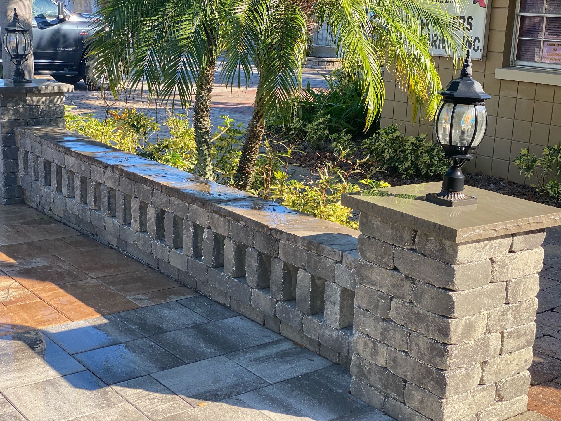 Stone garden wall with black lanterns beside a landscaped walkway and trees