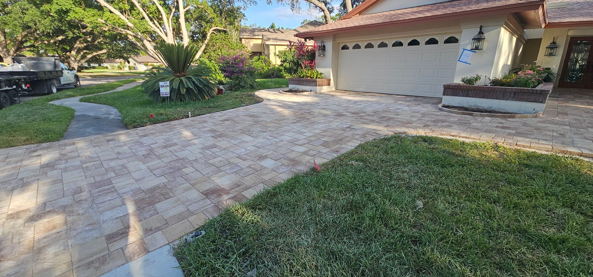 Suburban home driveway with a two-car garage, stone pavers, and a green lawn with trees.