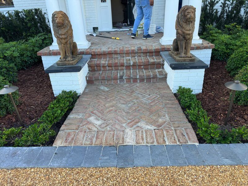 Brick walkway and steps leading to a front door, flanked by two stone lion statues on white pedestals.