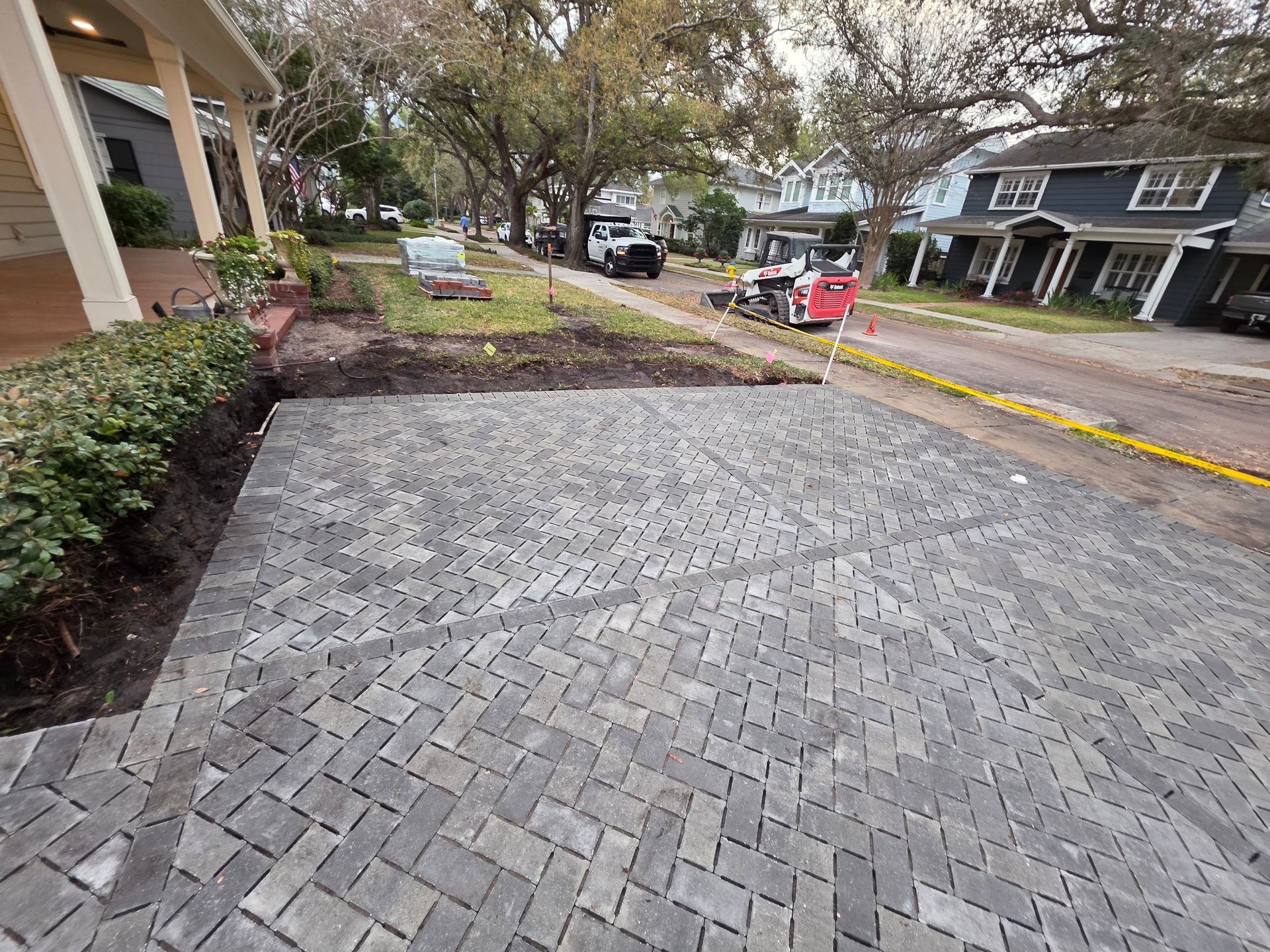 Brick-paved driveway beside a landscaped yard and residential street with parked cars