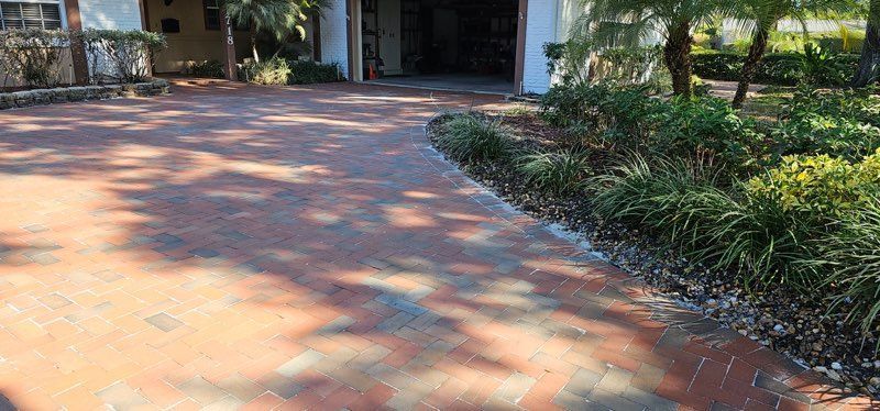 Sunlit brick driveway leading to a building entrance, bordered by landscaped greenery.