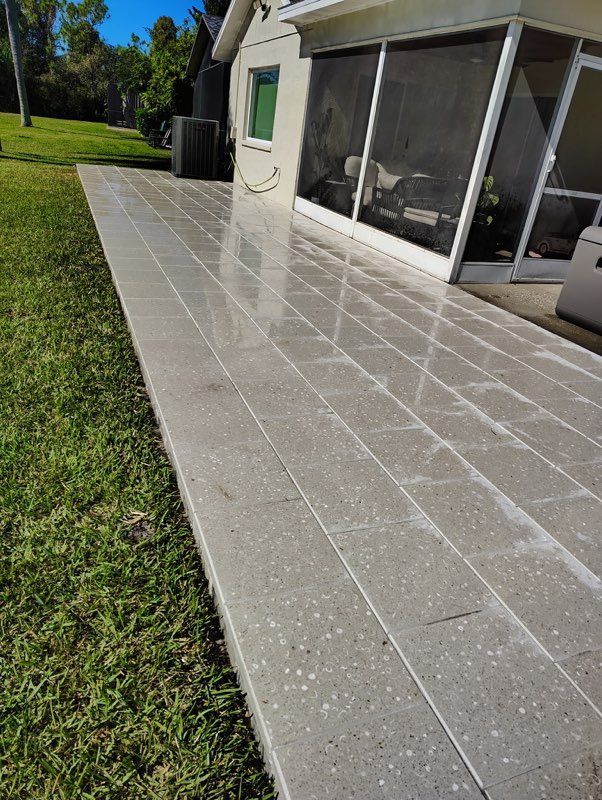Sunlit stone patio beside a house, with grass lawn and screened windows.