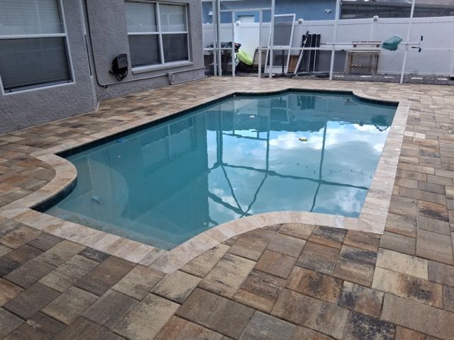 Backyard swimming pool with tan paver deck beside a house and screened patio