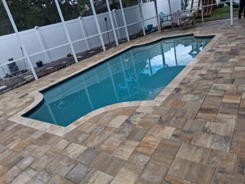 Backyard swimming pool beside a tan stone patio and white privacy fence
