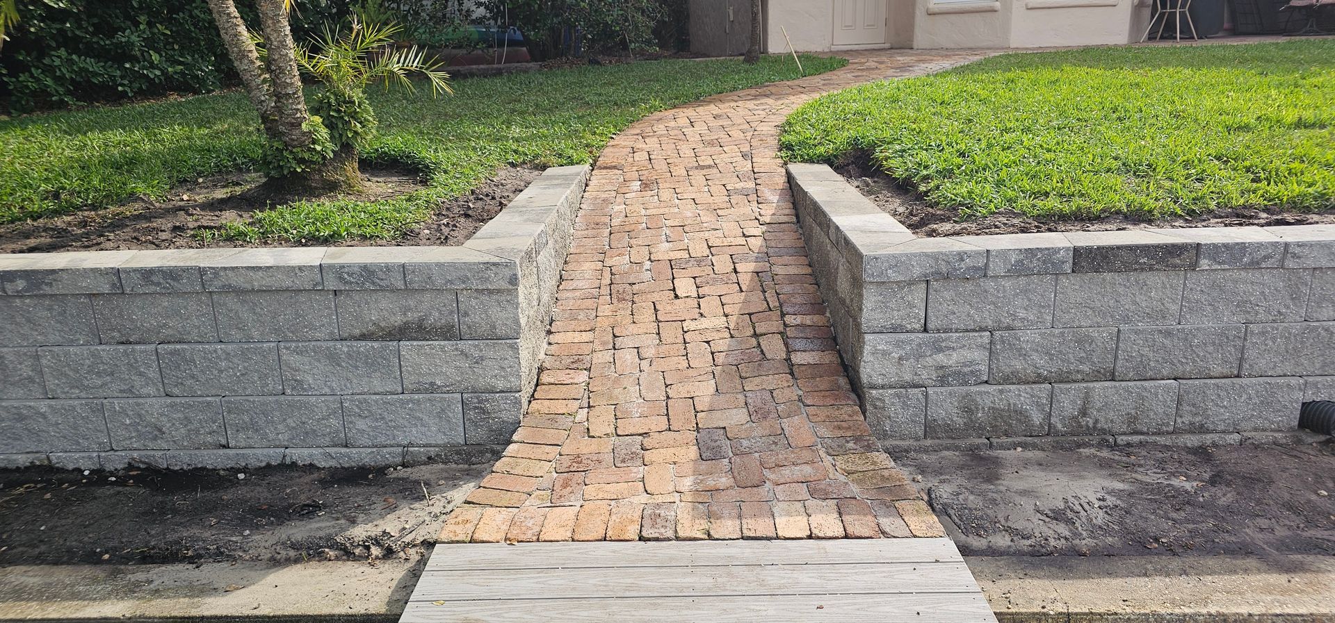 Brick walkway between raised concrete planters leading to a house entrance