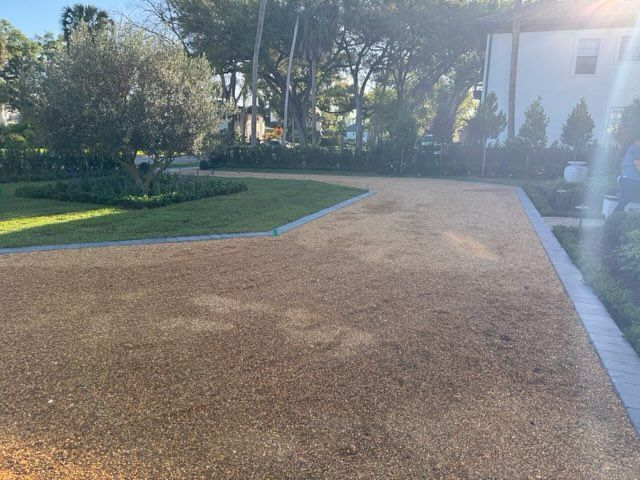 Gravel pathway beside a green lawn and trees in bright sunlight
