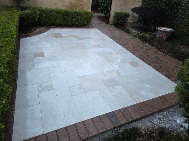 Stone-tiled patio with brick edging beside hedges and a garden path