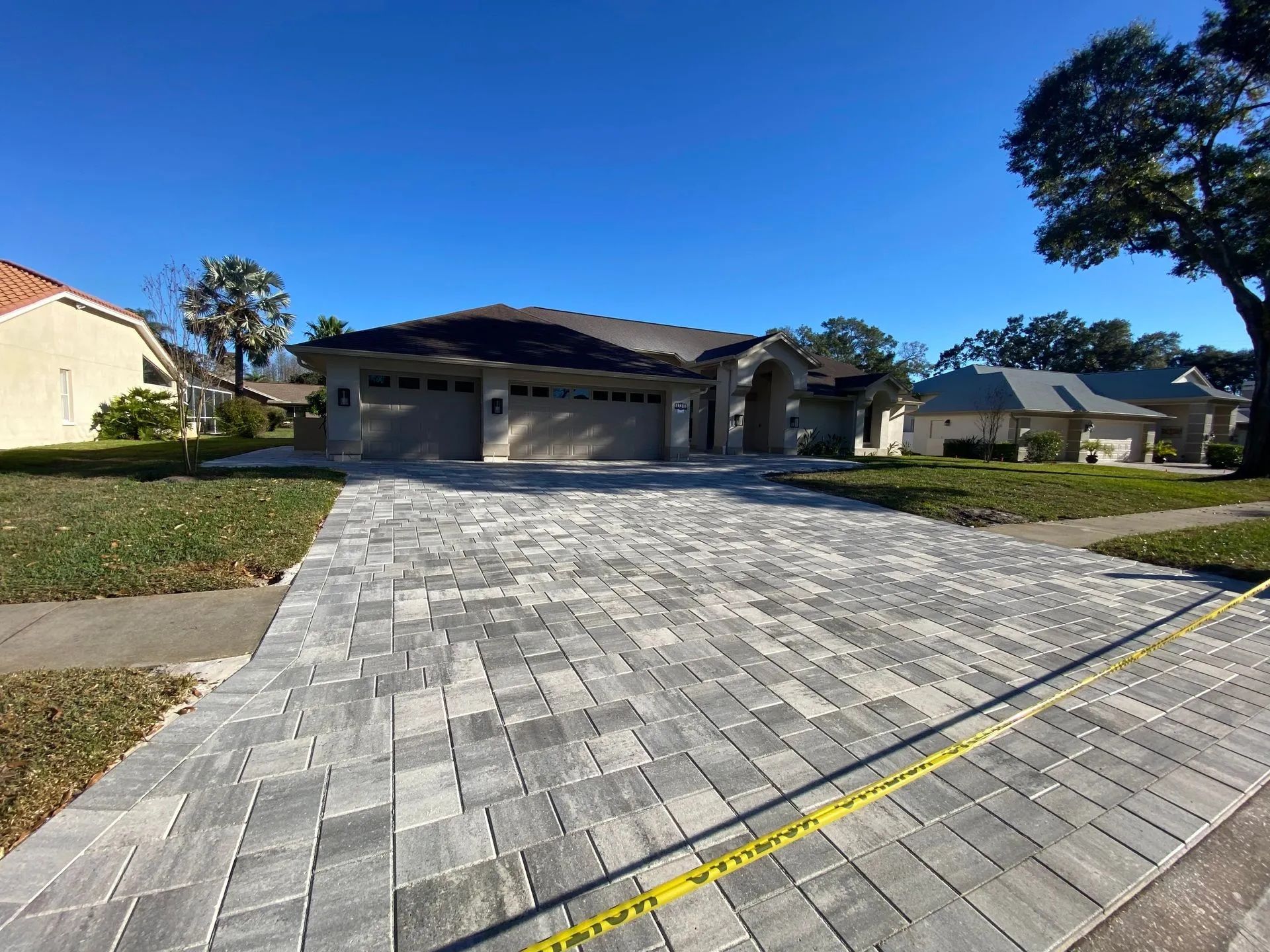 Modern single-story house with a long gray paver driveway under a clear blue sky