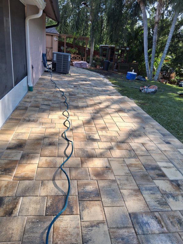 Backyard stone patio beside a house, with a garden hose running across it and trees and grass in the background