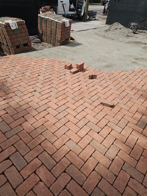 Brick paver walkway under construction with stacks of bricks and a small damaged section