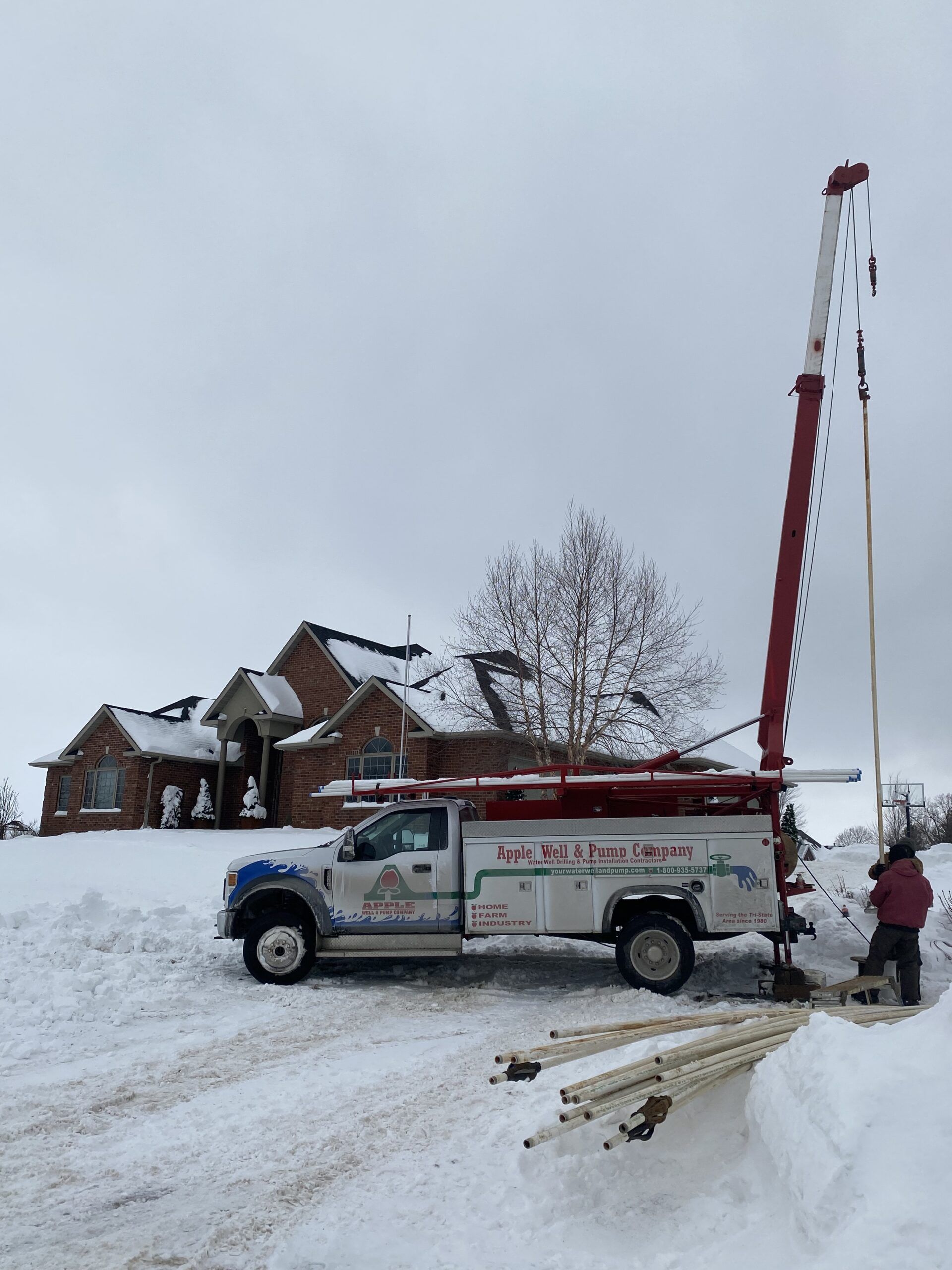Utility truck with raised boom in a snowy driveway beside a large house.