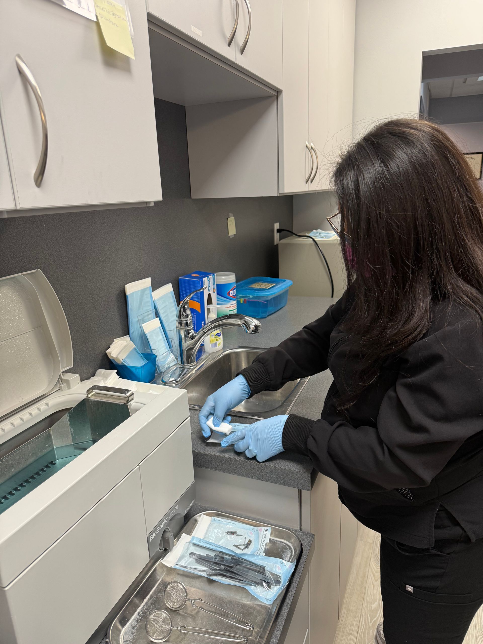 Person in gloves washing medical instruments at a dental clinic.