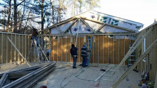 Construction workers framing a building; outdoor daylight setting.