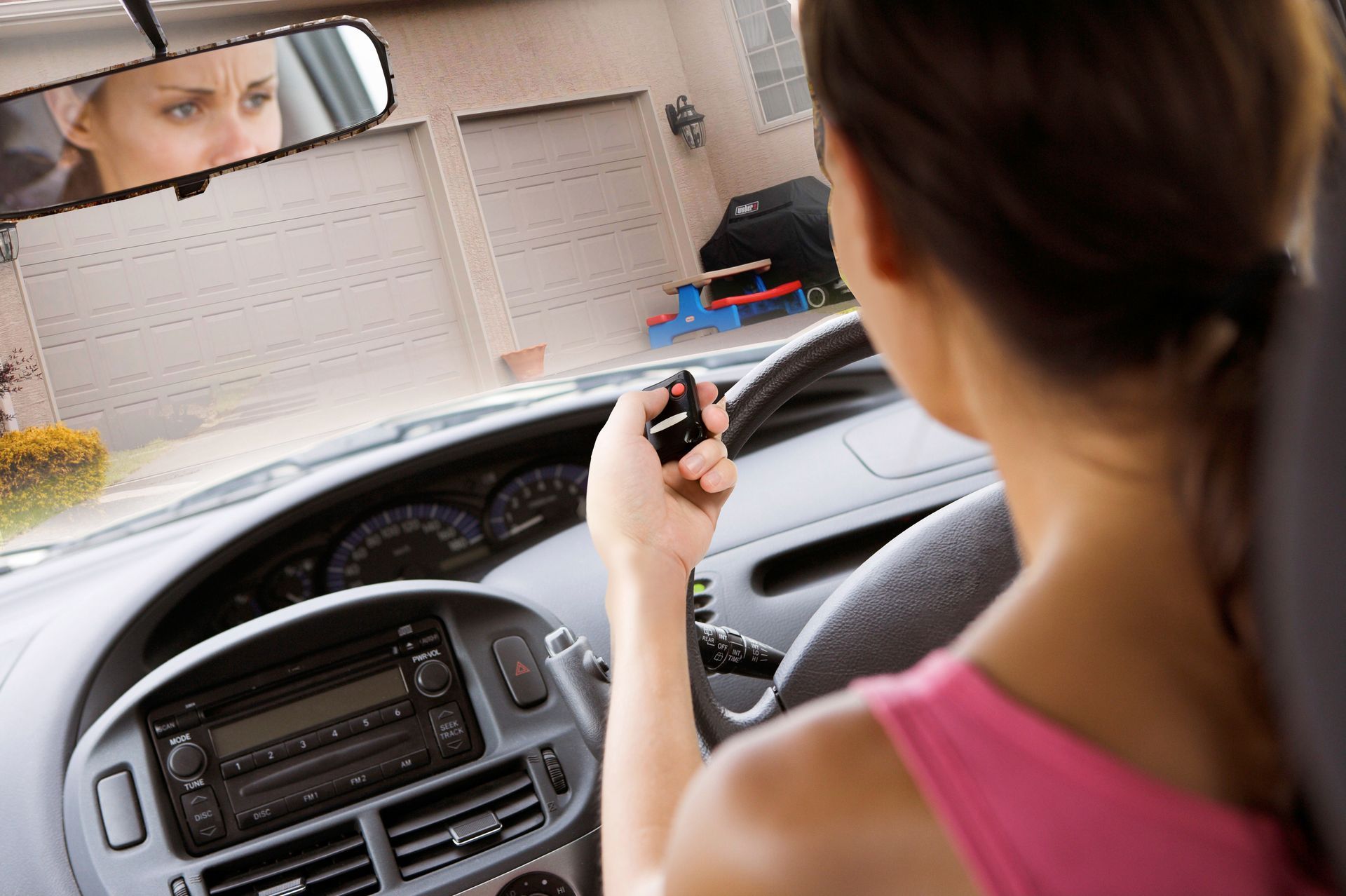 Woman in car using garage door opener; ajar garage door in background.