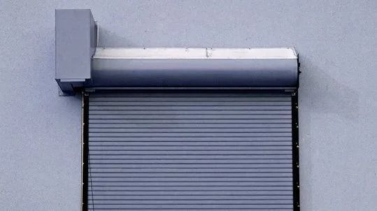 Gray rolling shutter partially lowered on a light blue wall.