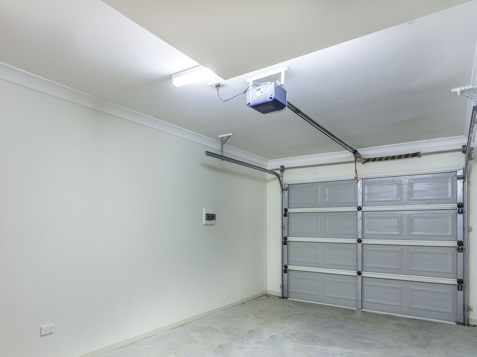 Empty garage interior with closed gray garage door and automatic opener on the ceiling.