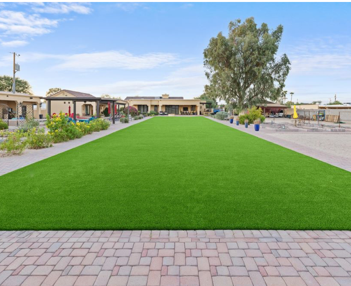 Bright green lawn bordered by brick paving and landscaped walkways in a courtyard with buildings and trees