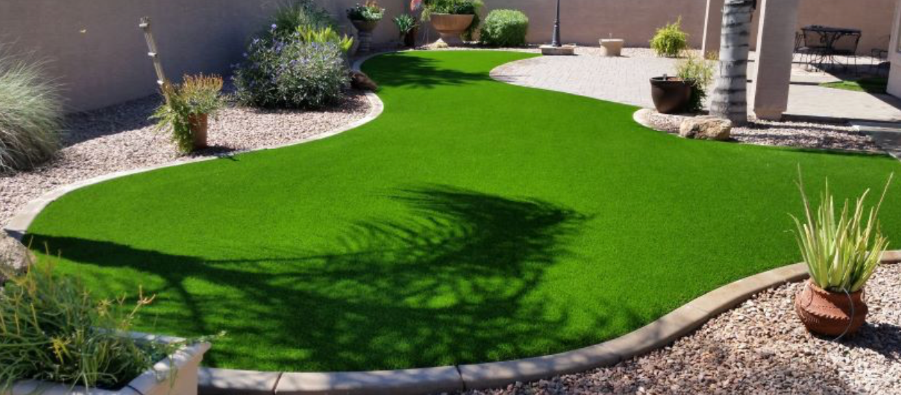 Bright green artificial turf courtyard with curved stone edging and desert plants in pots and beds