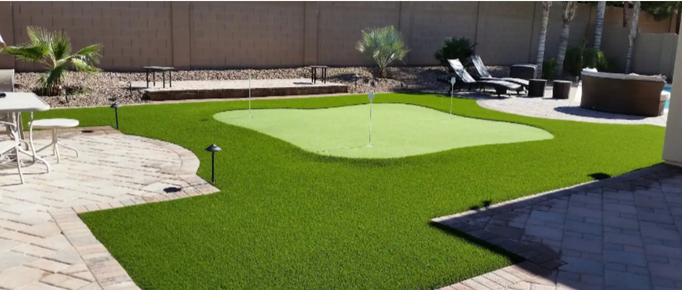 Backyard putting green with artificial turf, patio pavers, and a putting hole near a fence.