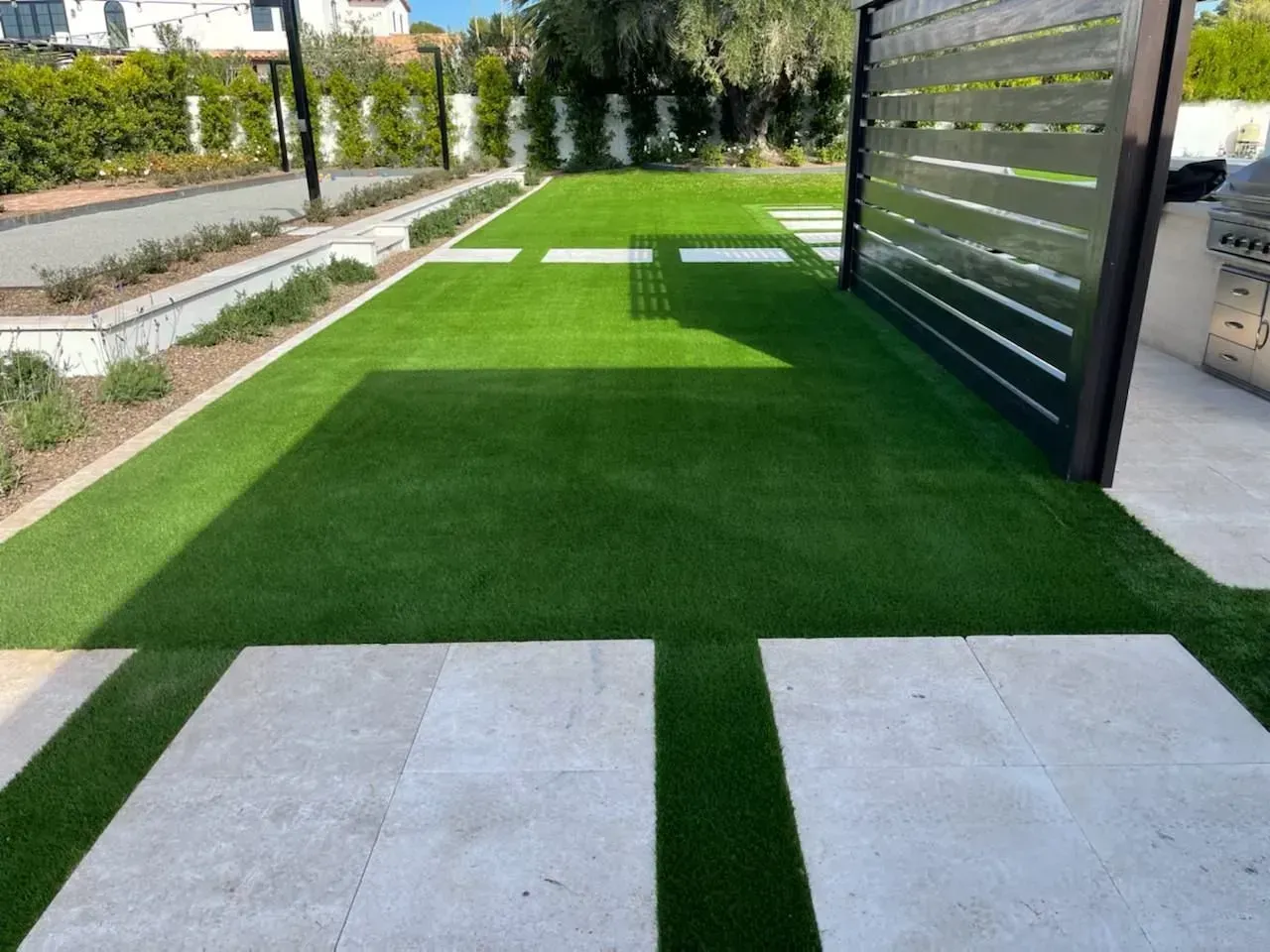 Modern outdoor walkway with artificial grass, stone pavers, and a slatted privacy screen