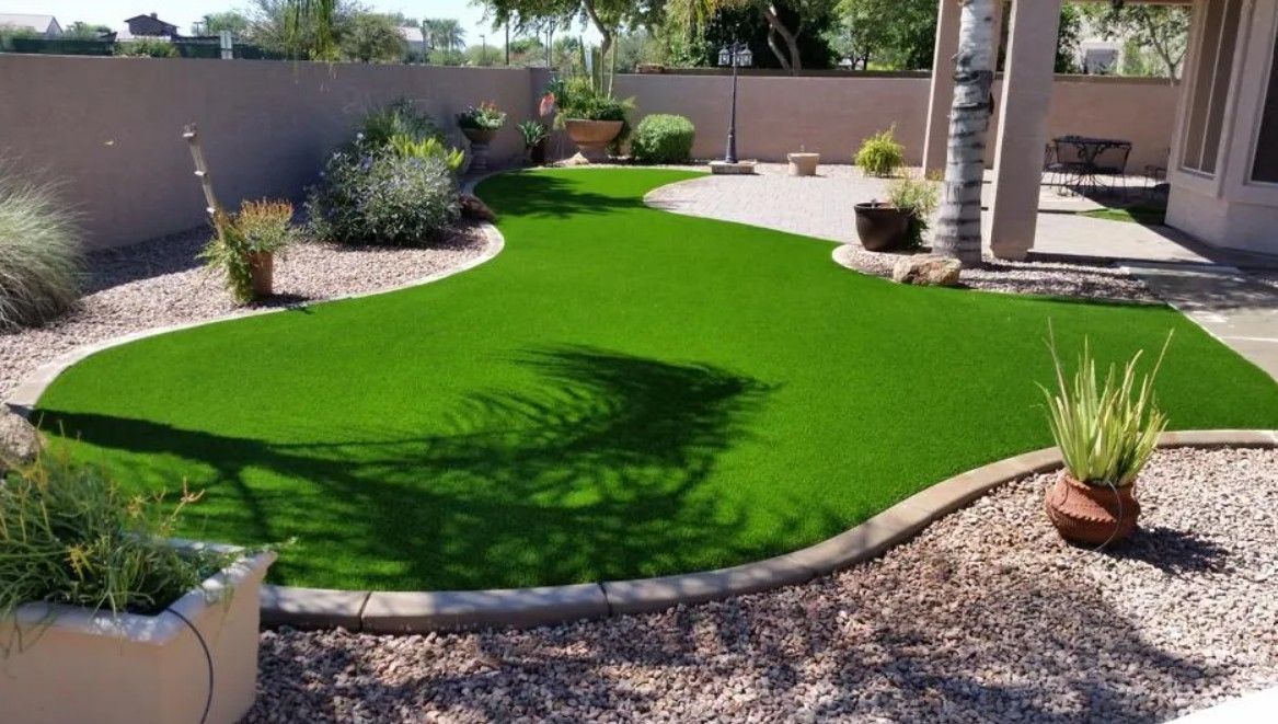 Backyard patio with bright green artificial turf, gravel borders, and potted plants under a shaded pergola