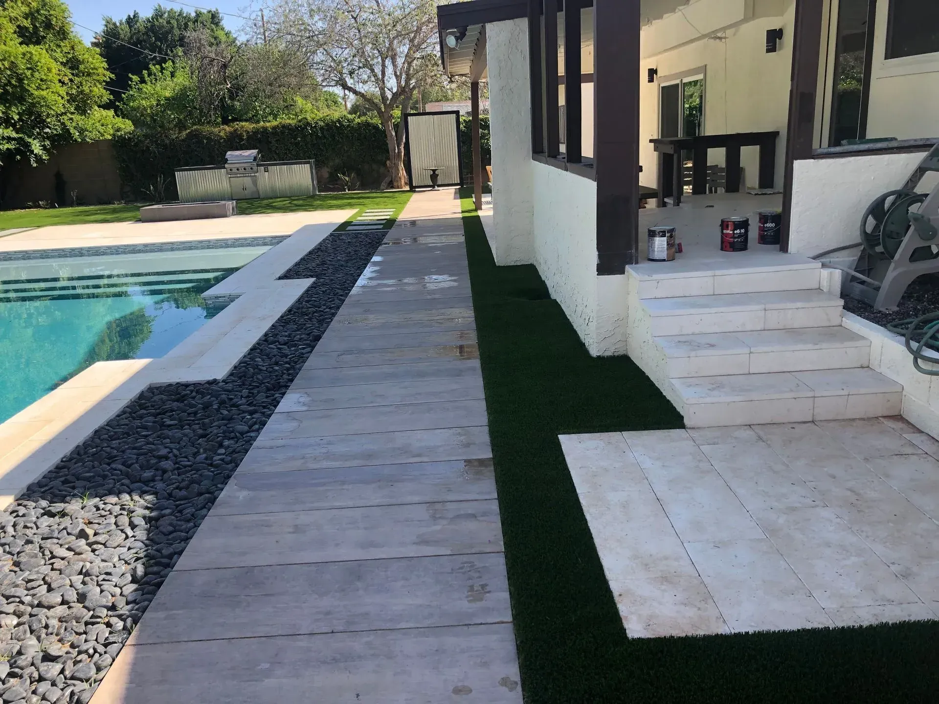 Backyard pool beside a modern patio with steps, lounge chairs, and a lawn strip.
