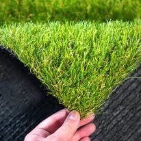 Hand holding the corner of a green artificial grass mat on a black backing