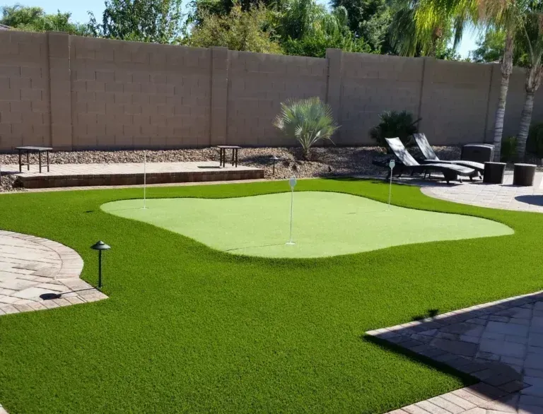 Backyard putting green with artificial turf, sand trap, lounge chairs, and a patio in the sun