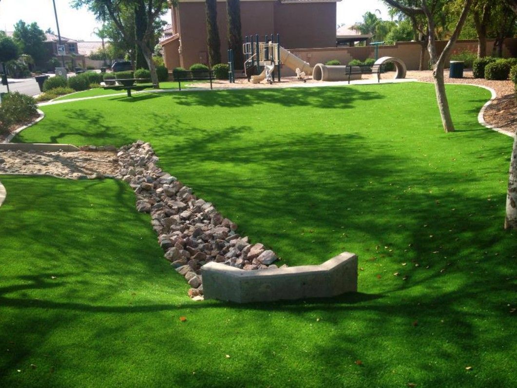 Landscaped lawn with bright green grass, stone border, trees, and a building in the background