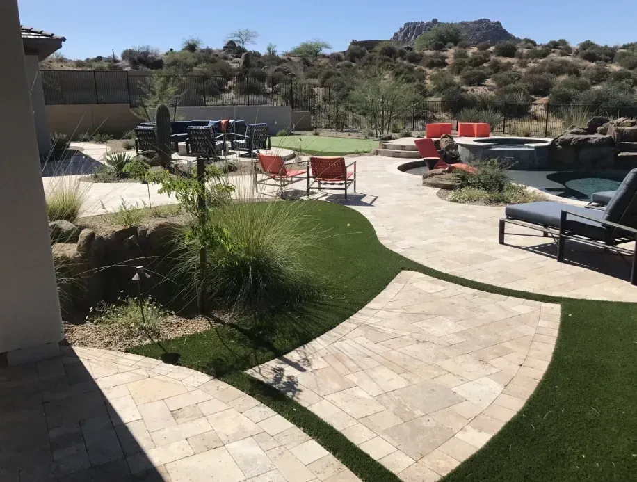 Patio with curved stone walkway, green lawn, and red lounge chairs beside a pool in a sunny backyard
