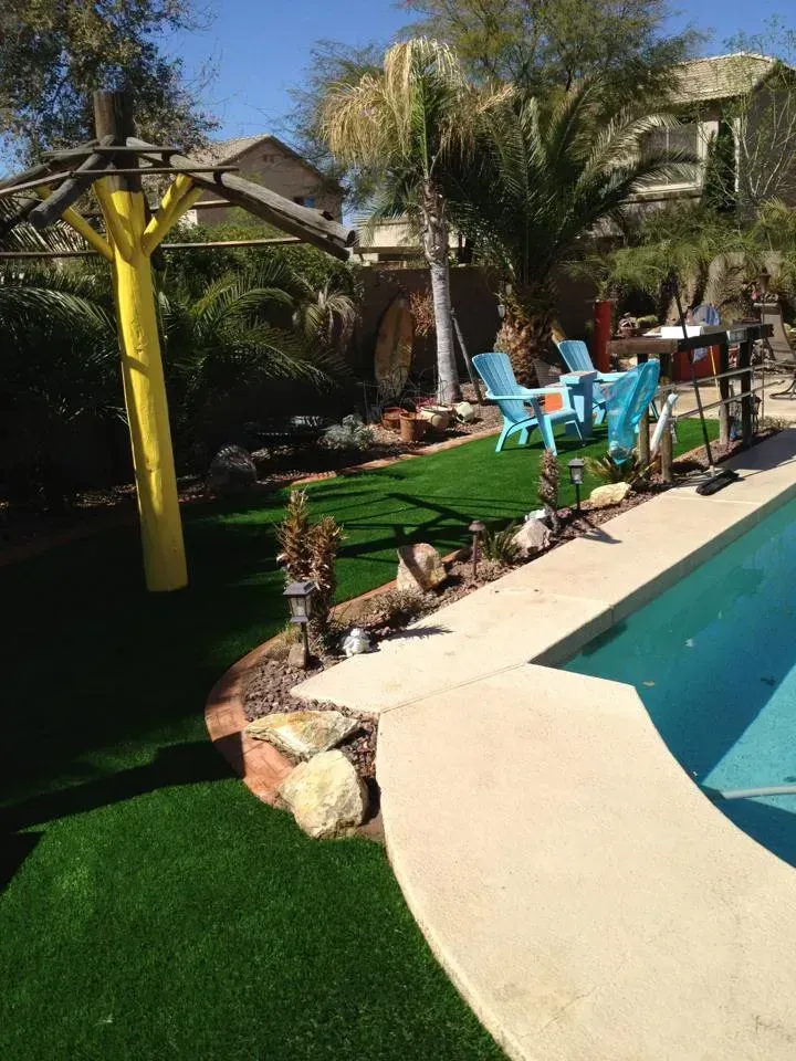 Backyard pool with turquoise water, blue chairs, palm trees, and a lawn under bright sun