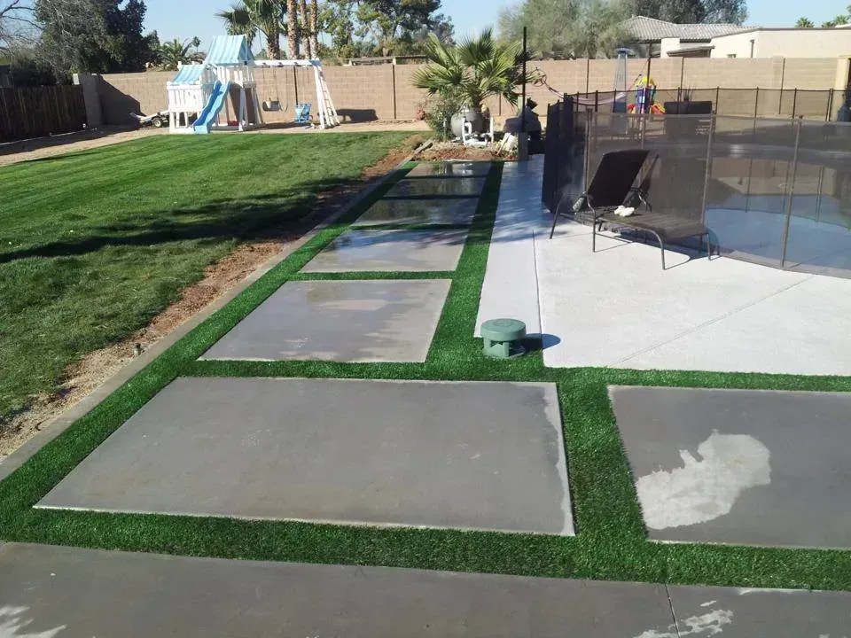 Backyard with patio, stepping stones, pool fence, and green lawn under bright sunlight