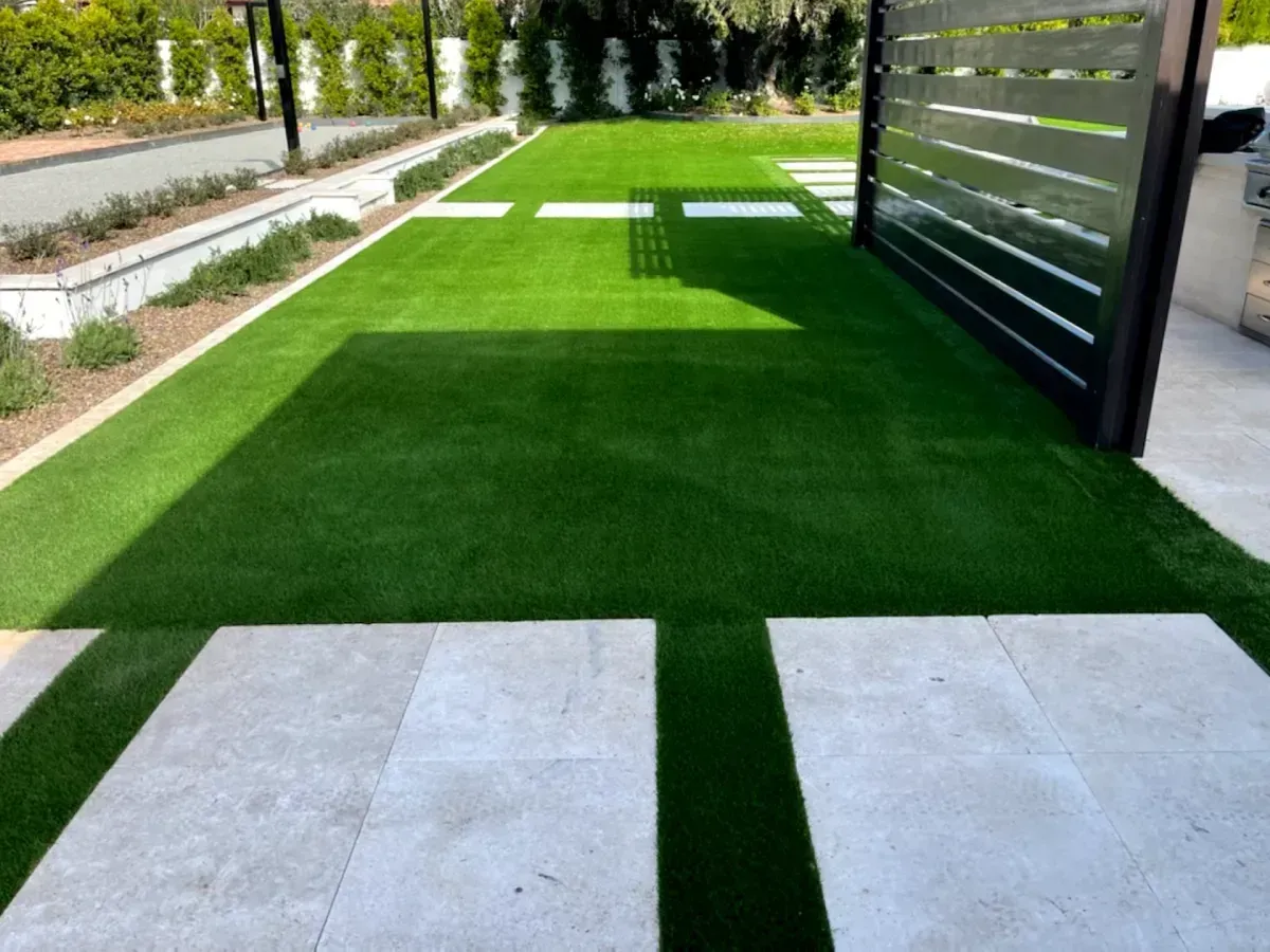 Green artificial turf walkway beside a dark slatted fence, with stone pavers in the foreground
