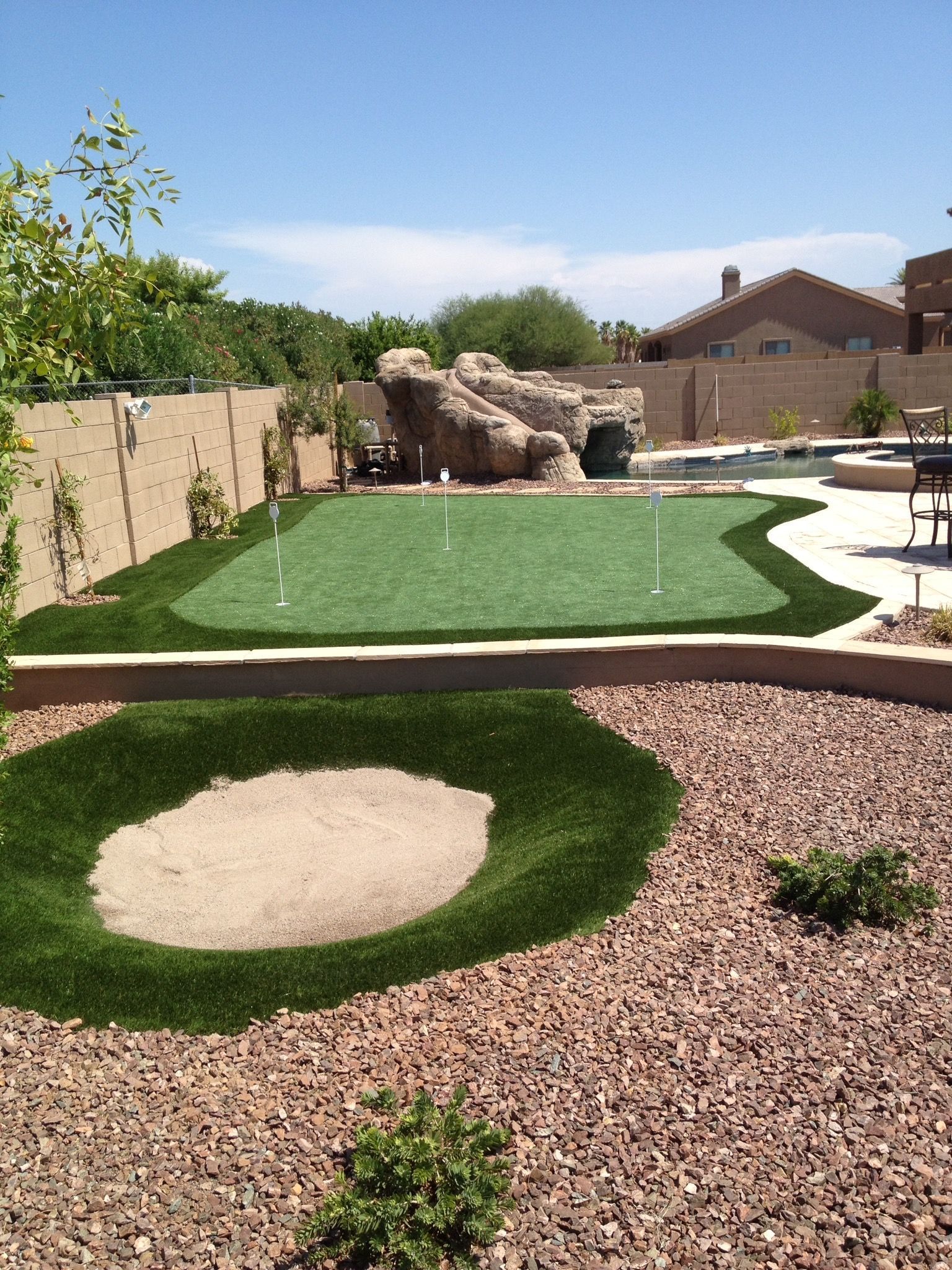 Backyard with artificial turf, sand bunkers, and a putting green under a clear sky