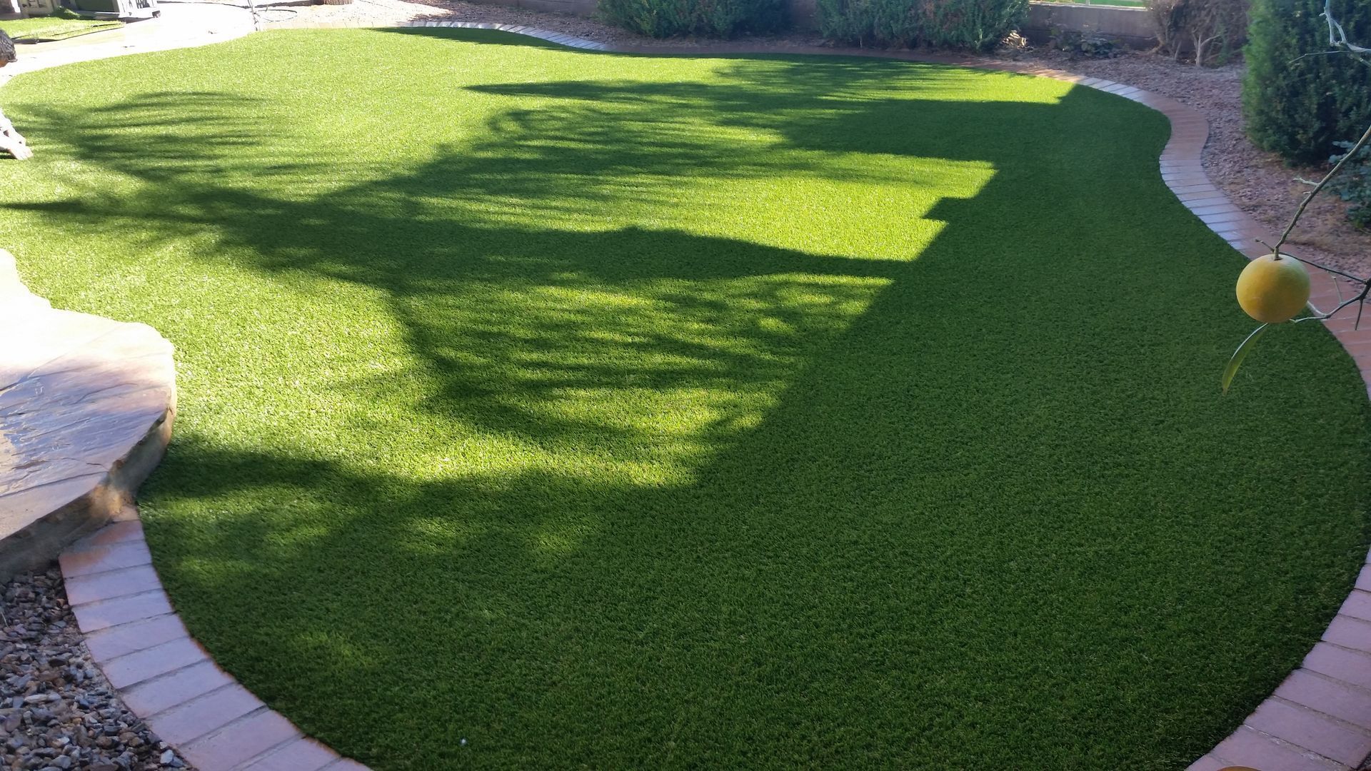 Curved green artificial lawn with stone edging and tree shadows in a sunny yard