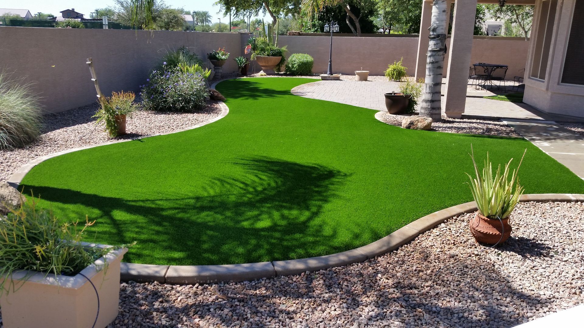 Curved bright green lawn in a landscaped backyard with gravel borders, shrubs, and a patio area