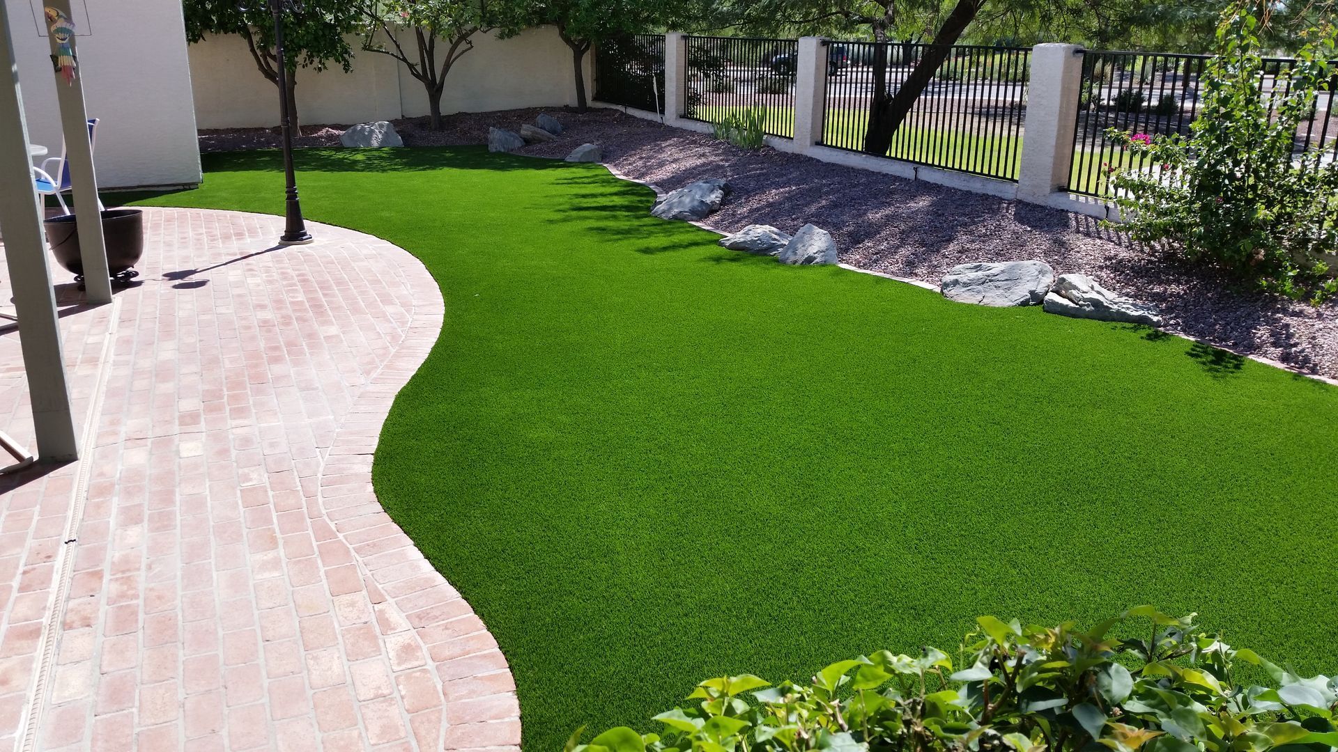 Curved brick walkway beside a bright green lawn and landscaped trees in a park-like yard