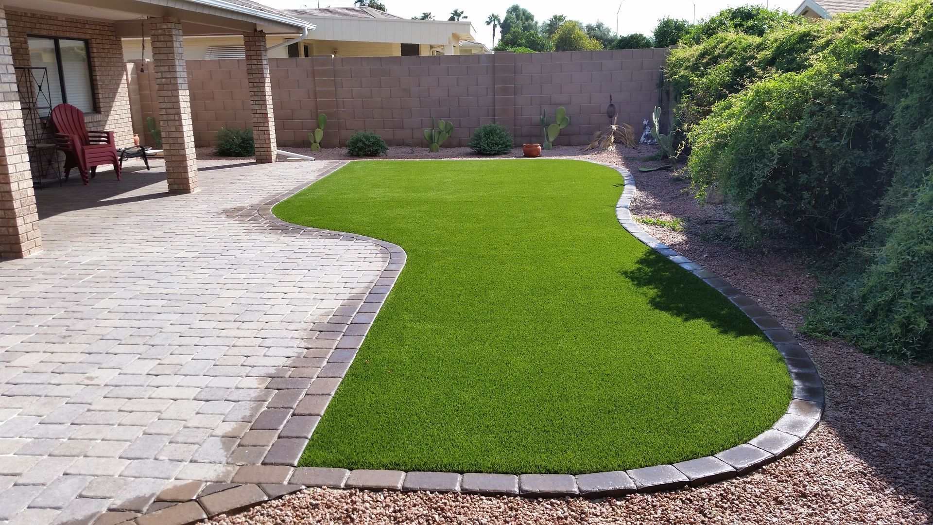 Backyard patio with curved green lawn, stone pavers, and shrubs along a wall