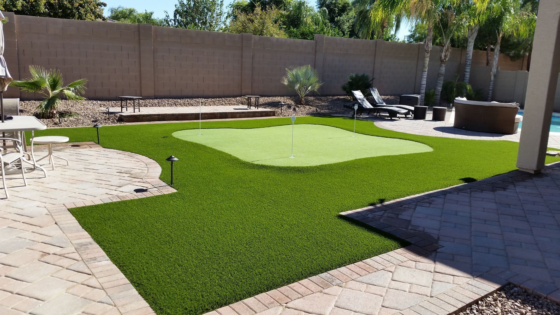 Backyard putting green with two golf putters, stone patio, and a fence in the background