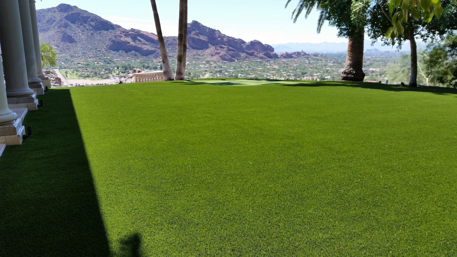 Bright green lawn under trees with mountains in the background and a clear sky