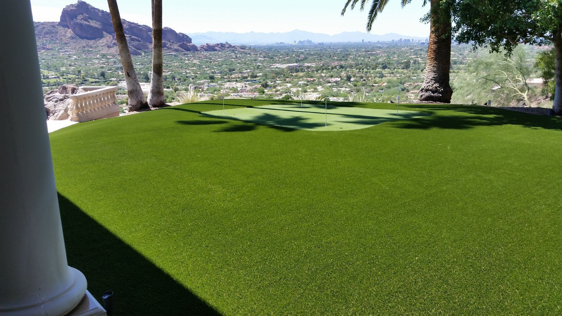 Shaded green lawn with palm trees overlooking a city and mountains in the distance