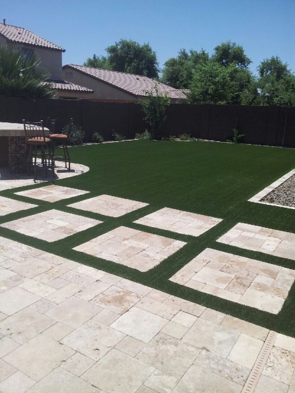 Backyard with green lawn, stone path, patio, and house under a clear sky