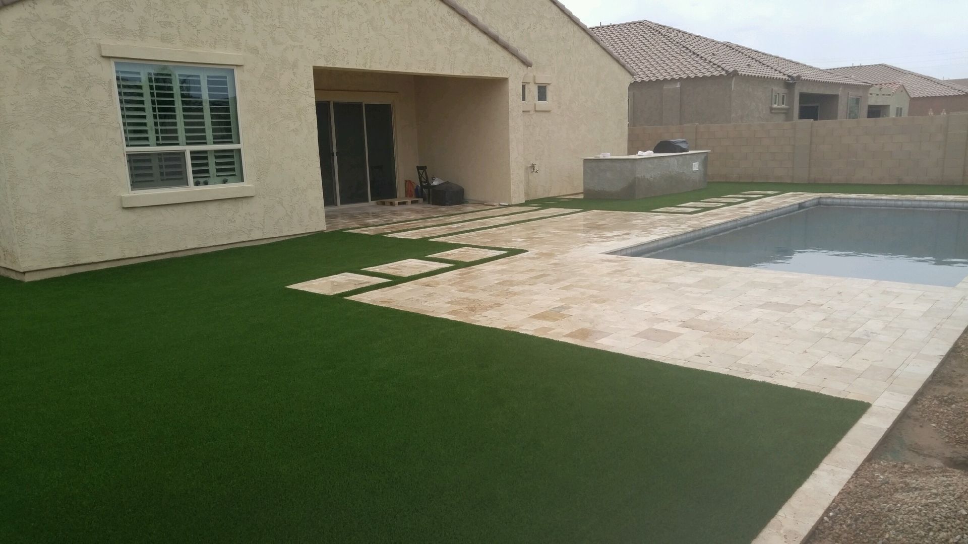 Backyard patio with artificial grass, covered seating area, and a swimming pool beside a house