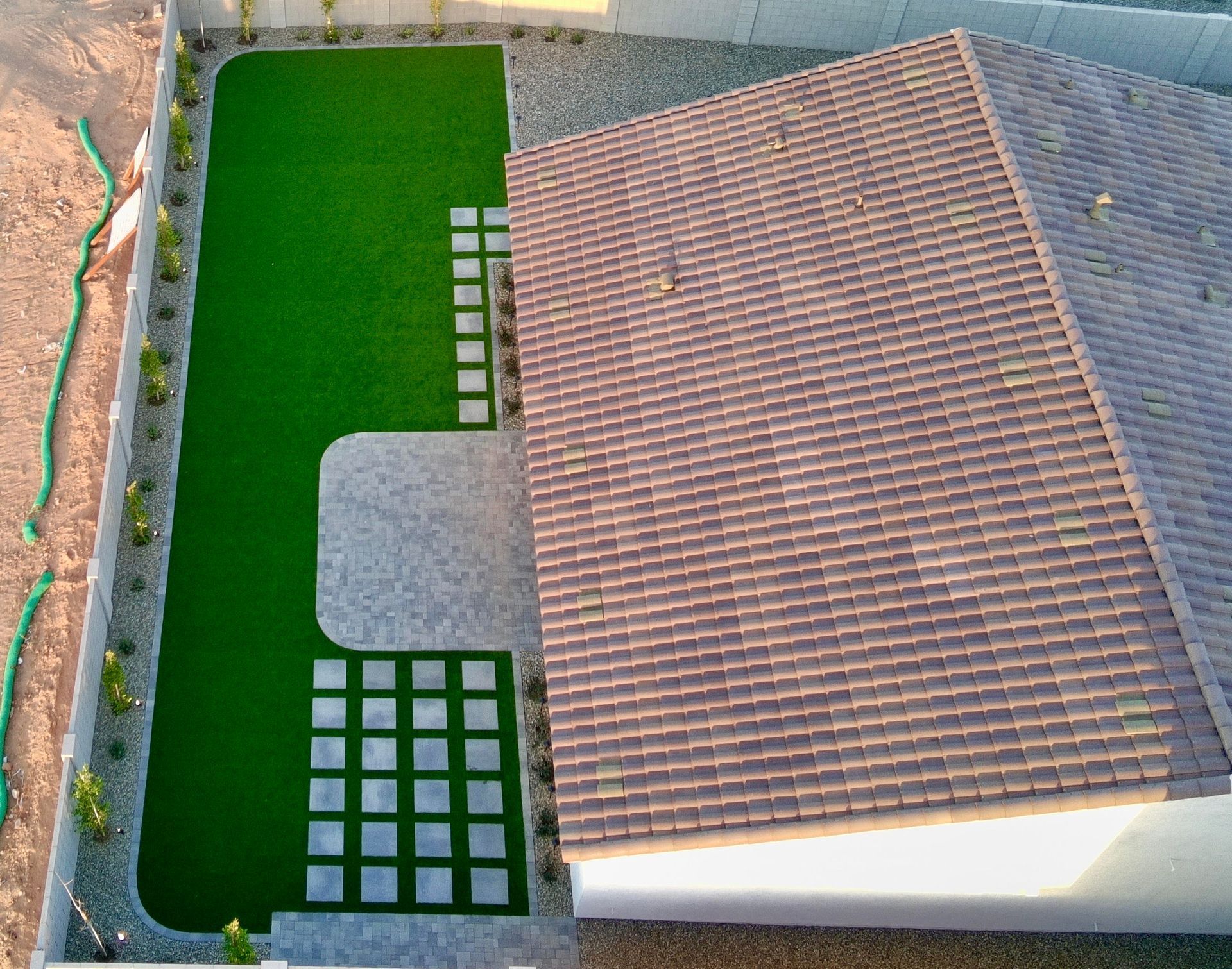 Aerial view of a house roof beside a green artificial turf yard with stone pavers.