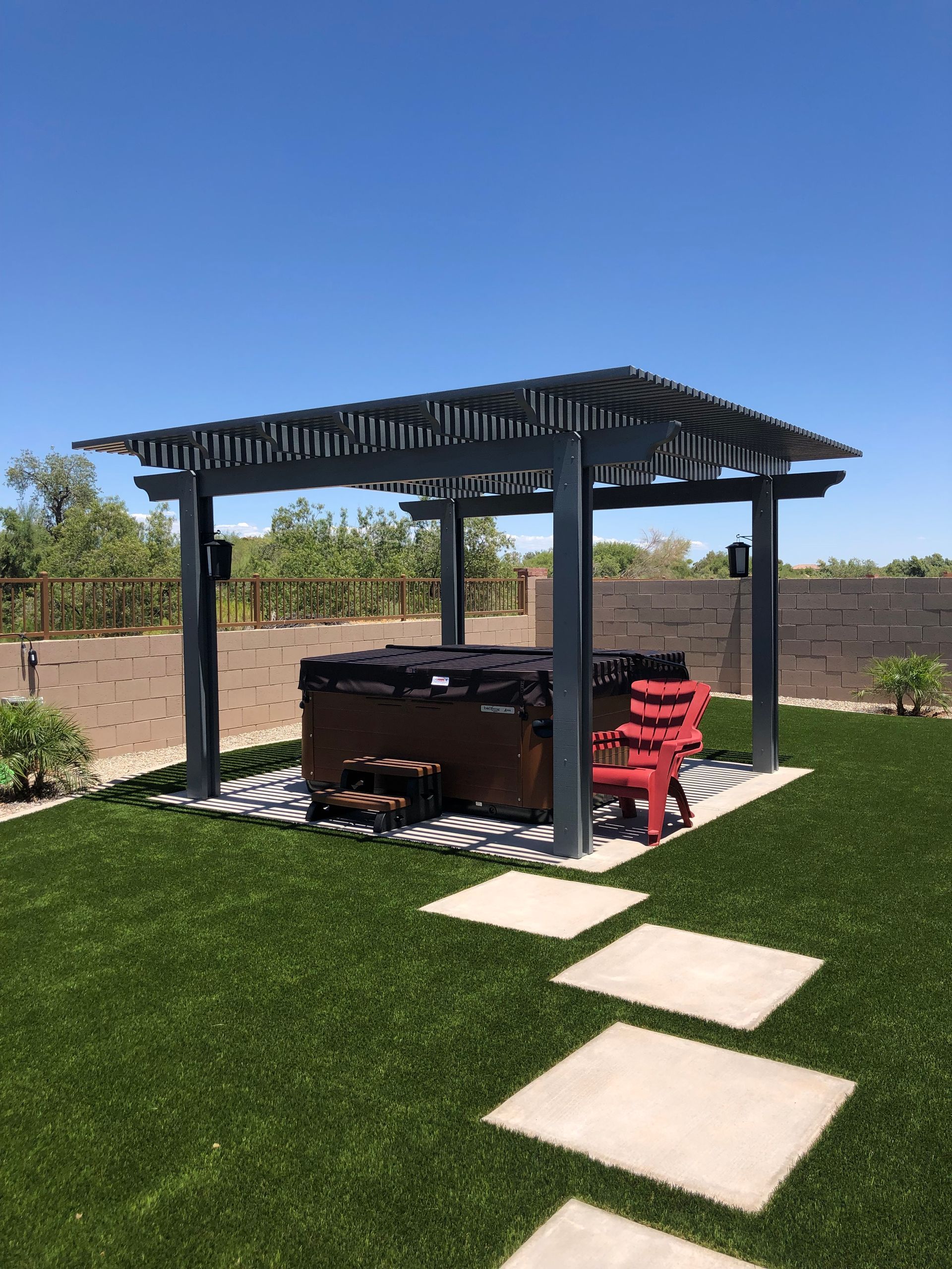 Backyard pergola with hot tub, red chairs, and stepping stones on green lawn