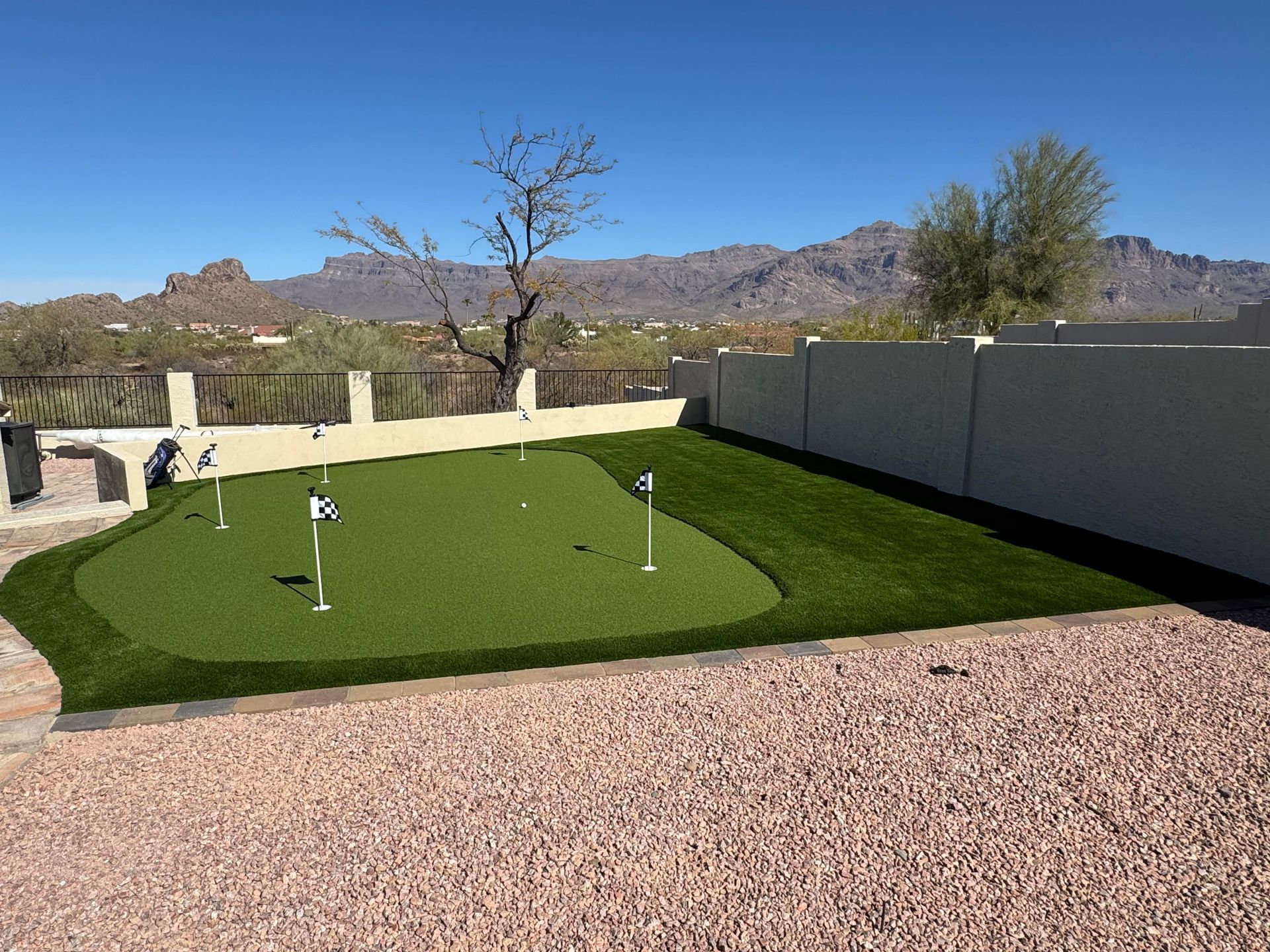 Backyard putting green with flags, gravel border, and desert mountains in the background