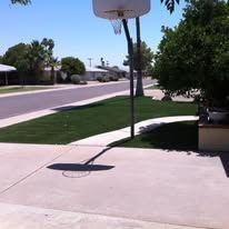 Basketball hoop over a sunlit driveway beside a quiet suburban street and green lawn