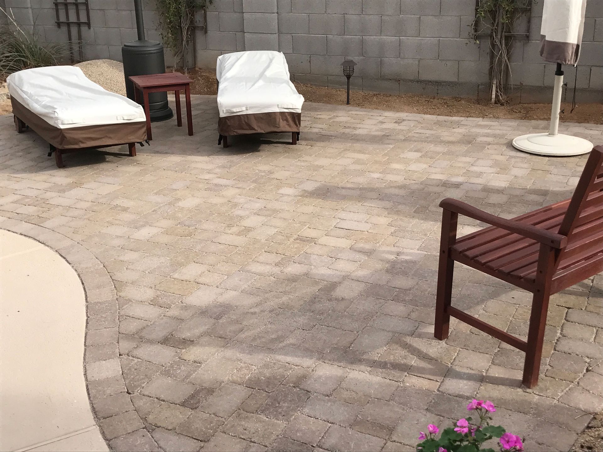 Patio with wicker chair, covered loungers, table, umbrella base, and pink flowers on pavers