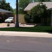 Suburban house with a white car in the driveway, palm tree, and manicured lawn beside the street